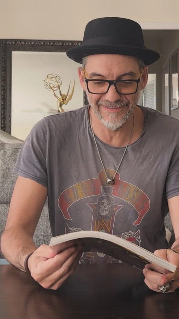 Alessandro Taini reading his own artbook at his table, his Emmy on the shelf behind him