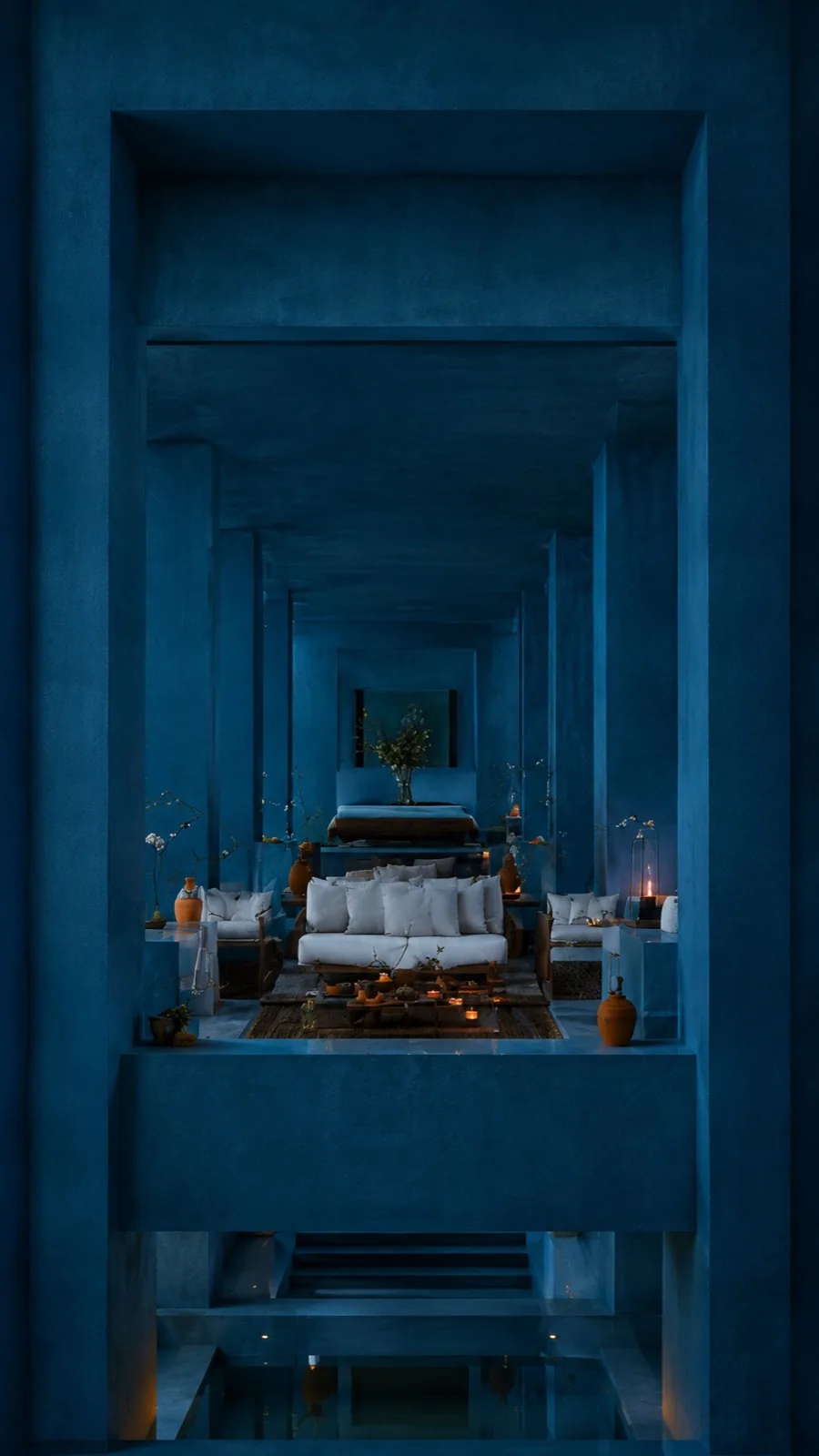 Blue corridor of receding portals framing a candlelit lounge with white cushions, terracotta vessels and a low carved table at the far end.